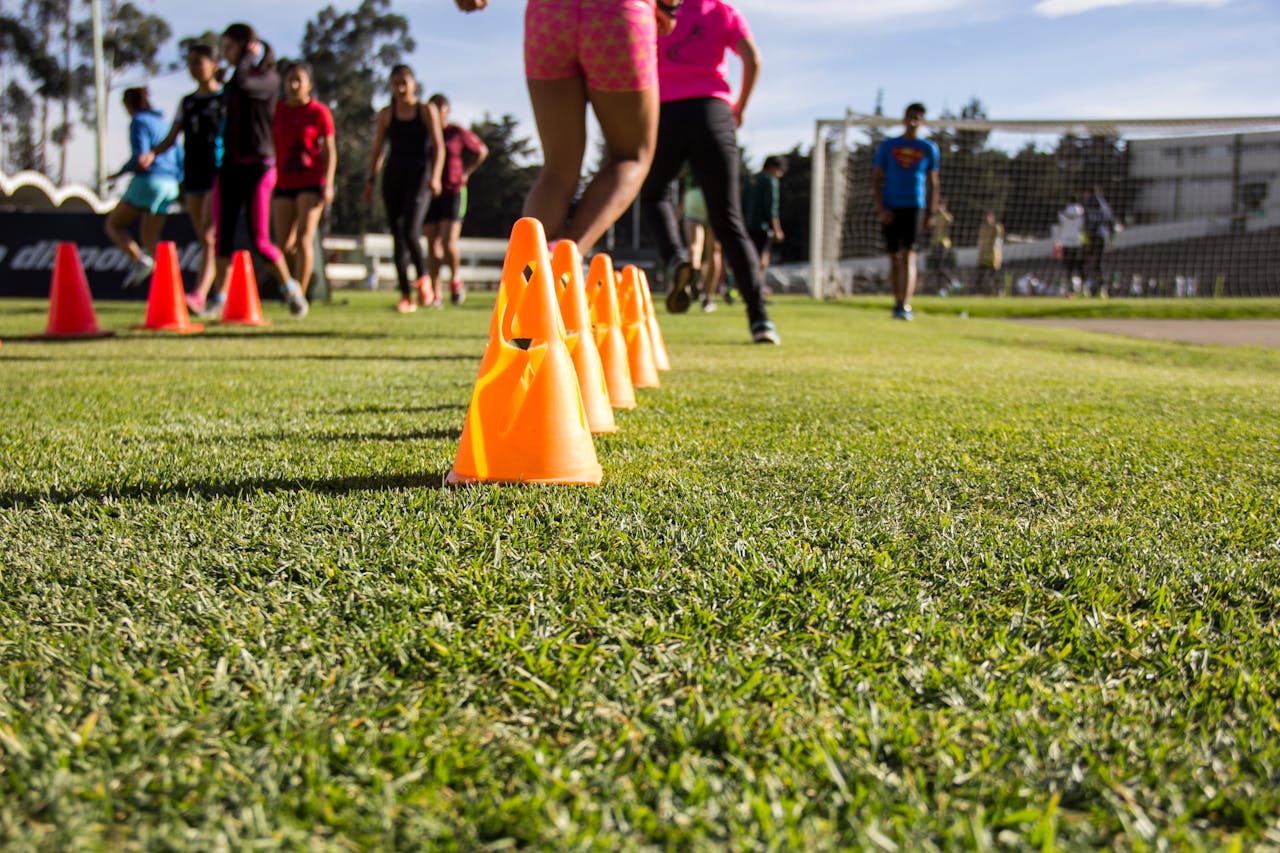 Dynamic soccer training session with teenagers practicing agility using orange cones on grass field.